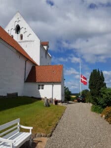 Kirke med flag på halv og rustvogn foran
