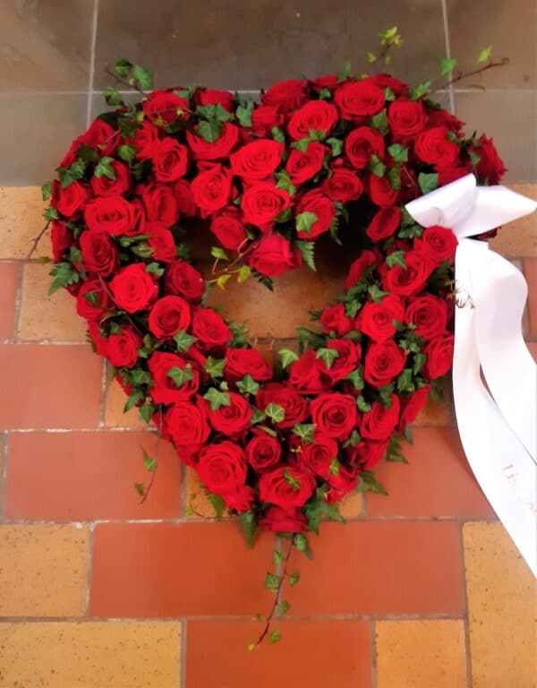 klassisk kistepynt i et hjerteformet oasis m. røde roser og bånd