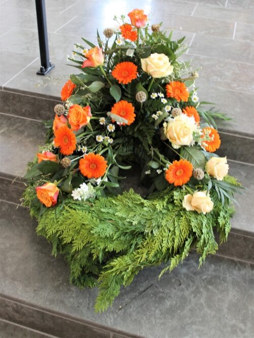 Begravelseskrans med høj blomsteropsats på krans af thuja i orangefarvede toner