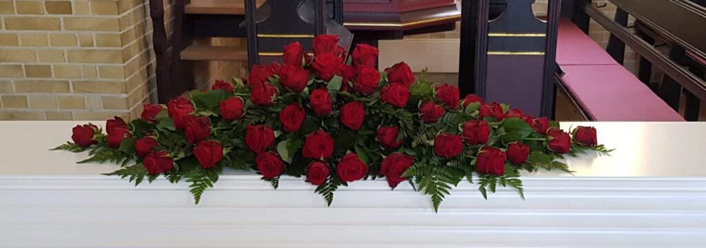 Røde roser på hvid kiste ved begravelse Tommerup kirke