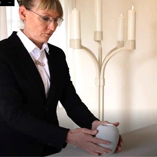 Bedemand Joan Holst fra Glamsbjerg stiller tændt mindelys på hvid kiste