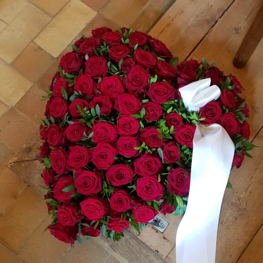 Hjerte af røde roser med hvidt bånd lagt af bedemand i Hårby