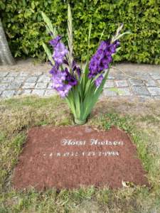 gravsten og plænesten i græsplæne med buket af lilla blomster