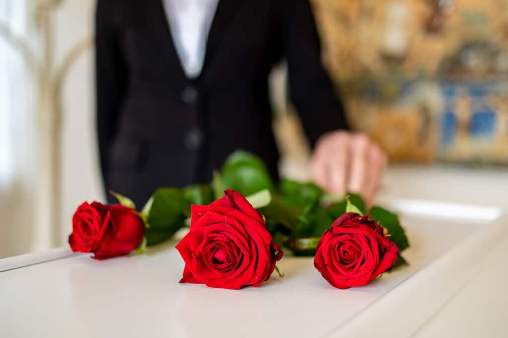bedemand Joan Holst lægger tre røde roser på hvid kiste