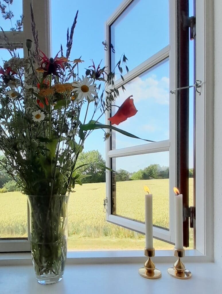 Vase med buket af vilde blomster og stearinlys i vindueskarm